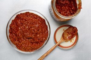 A bowl of chili next to two jars and a spoon.