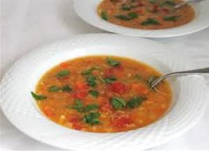 A bowl of soup with tomatoes and spinach.