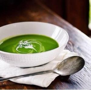 A bowl of green soup with spoon and napkin.