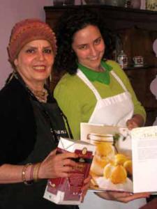 Two women holding a cookbook and ingredients.