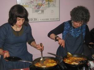 Two women are cooking food in a pan.