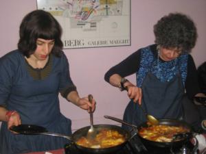 Two women cooking food in a pan on the stove.