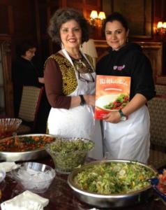 Two women standing in front of a table full of food.