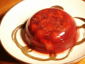 Red gelatin dessert with cherries on plate.