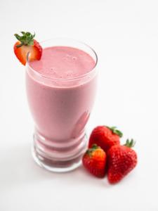 A glass of strawberry smoothie with strawberries on the side.
