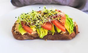 A sandwich with avocado, tomato and sprouts on it.