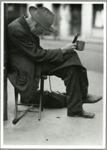 Man sitting with hat, holding a cup.