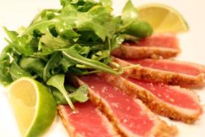 Seared tuna with greens and lime wedges.