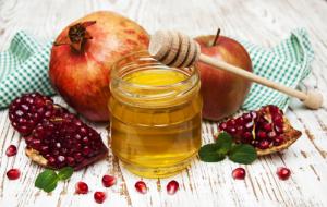 A jar of honey surrounded by pomegranates and apples.