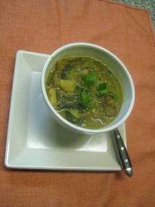 Bowl of soup with herbs on plate.