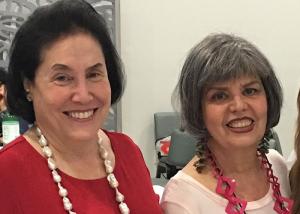 Two women wearing necklaces and smiling for a picture.