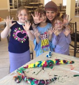 Children with paint-covered hands at art table.