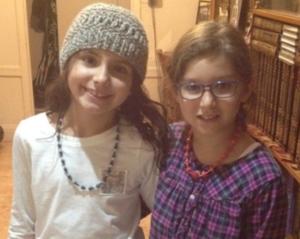 Two girls smiling indoors, wearing necklaces.