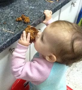 Toddler reaching up to eat cookie.