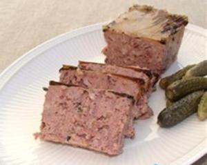 Sliced meatloaf with pickles on plate.