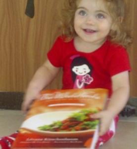 A little girl sitting in front of a box of food.