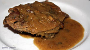 A piece of meat is on the plate with gravy.