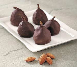A white plate topped with chocolate covered pears next to almonds.