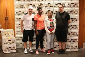 Four people standing before stacked plastic crates