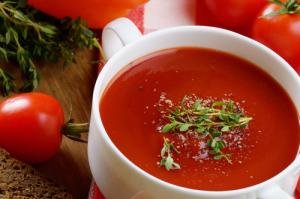 A bowl of soup with tomatoes and herbs in it.
