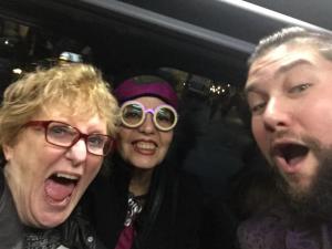 Three people are taking a selfie in the back of a car.