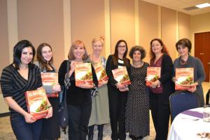 A group of women holding up books in front of a wall.