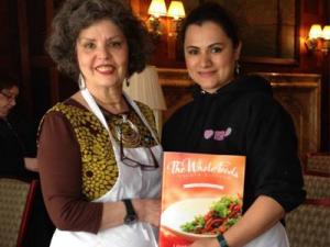 Two women holding a cookbook in front of each other.
