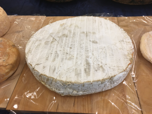 A round cheese sitting on top of a wooden board.