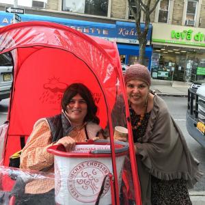 Two people standing under a red umbrella on the street.