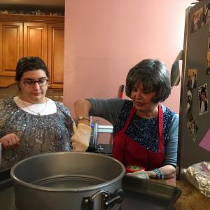 Two women in aprons and a pot on the counter.