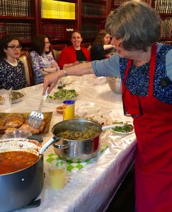 A woman in red apron standing at table with food.