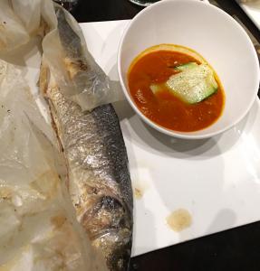 A bowl of soup and a fish on the table.
