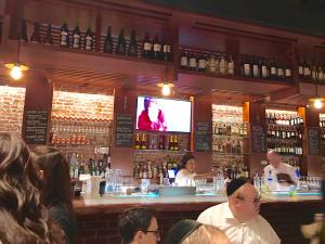 A group of people sitting at a bar watching television.