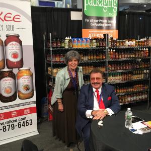 A man and woman sitting at a table in front of a sign.