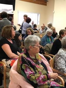 A group of people sitting in chairs and some are standing up.
