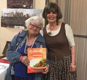 Two women standing next to each other holding a book.