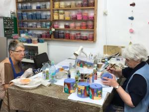 Two women painting decorative cylinders at table