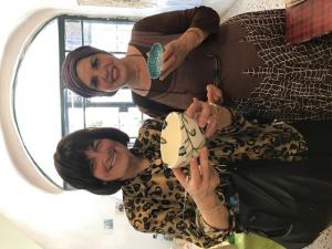 Two women standing next to each other holding a cake.