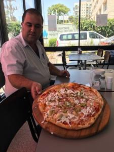 A man standing in front of a pizza on top of a table.