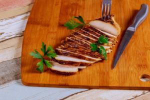 A wooden cutting board with meat and utensils on it.