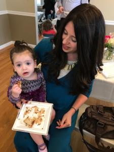 A woman holding a cake with a baby in front of her.
