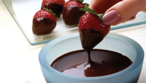 A person dipping strawberries into chocolate.