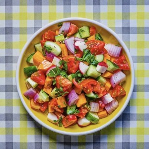 A bowl of salad on a checkered table cloth.