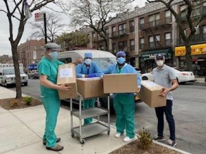 Three people in scrubs and masks are holding boxes.