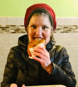 A woman in black jacket eating food on white napkin.