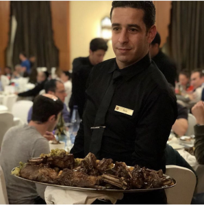 A man holding a tray of food in front of people.