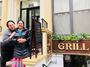 Two women standing outside of a restaurant with the grill sign in front.