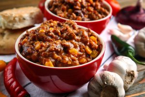 Two bowls of chili on a table with peppers.