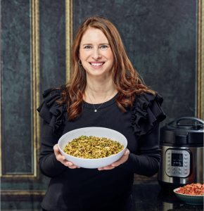 A woman holding a plate of food in front of a coffee pot.