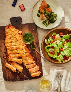 A wooden cutting board with some meat and salad